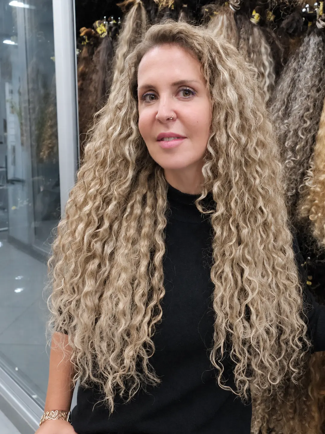 תוספות שיער לתלתלים אחרי: לקוחה אמיתית עם תלתלים בלונדיניים ארוכים ומלאים עד המותניים, מול תצוגת שיער מתולתל בסטודיו